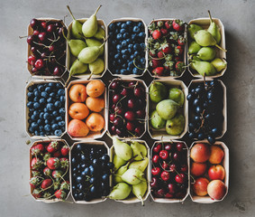 Summer fruit and berry variety. Flat-lay of strawberries, cherries, grapes, blueberries, pears, apricots, figs in wooden eco-friendly boxes over grey background, top view. Local farmers produce