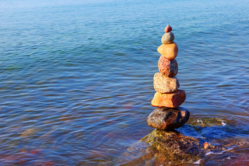 Rock zen pyramid of colorful pebbles standing in the water on the background of the sea