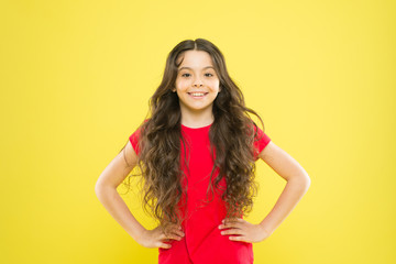 A perfect hairstyle. Little kid with cute smile and fashion hairstyle. Happy child with flowing hair on yellow background. Adorable small girl smiling with long wavy hairstyle. Hairstyle trends