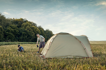 Family set up tent camp at sunset, beautiful summer landscape. Tourism, hiking and traveling in nature.