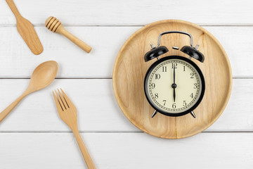 Top view of a wooden dish and eating utensils with a clock