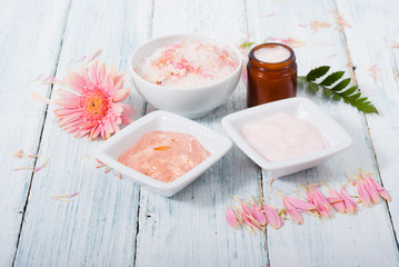 beauty product samples, cosmetic cream, bath salt, liquid soap and pink flower, white wood table