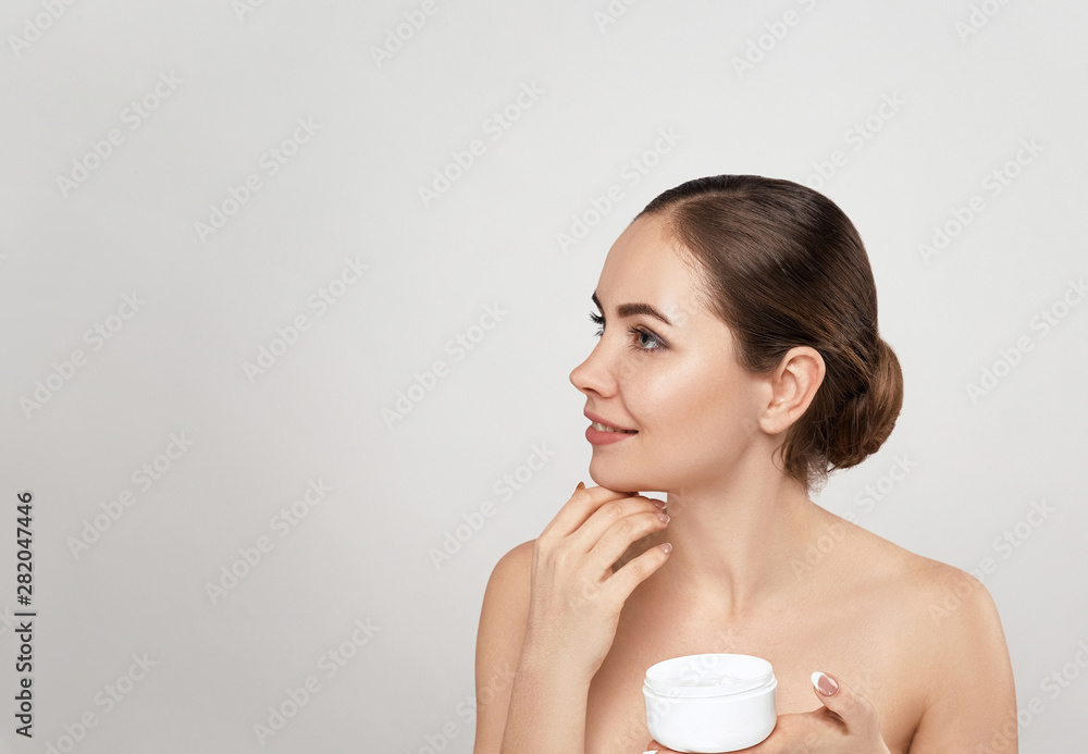 Wall mural Beautiful Woman With Face Cream. Skin Protection. SkinCare. Spa. A Young Female Holds Moisturizing Cream and Smiling. Natural Makeup