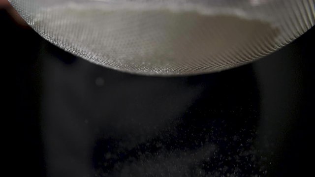 Flour is sifted through a sieve on black background