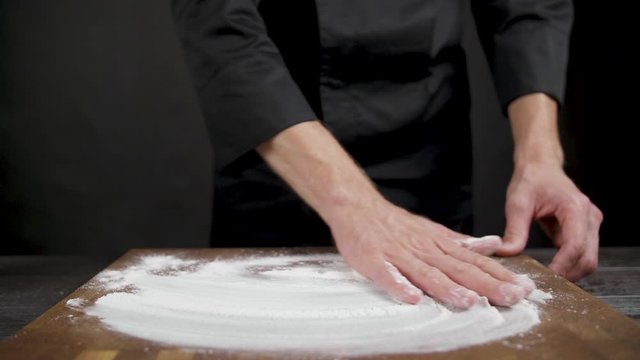 Cook spreads flour on wooden table on black background