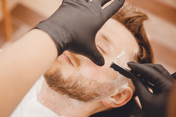 Obraz na płótnie Canvas Barber shaves beard of man in barbershop with razor