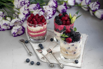 Healthy nutrition Dietary desserts. Glasses are filled with cottage cheese cream, in them chia seeds, raspberries, blueberries, blackberries. Near for background flowers.