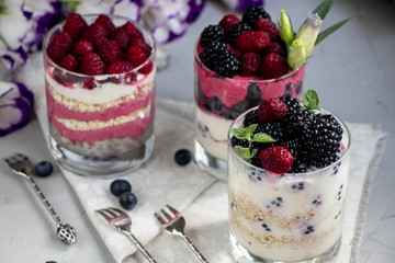 Healthy nutrition Dietary desserts. Glasses are filled with cottage cheese cream, in them chia seeds, raspberries, blueberries, blackberries. Near for background flowers.
