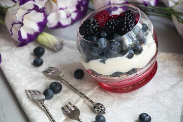 Healthy nutrition Dietary desserts. Glasses are filled with cottage cheese cream, in them chia seeds, raspberries, blueberries, blackberries. Near for background flowers.