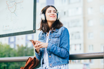 Smiling excited brunette woman wearing blue denim jacket with headphones looking away, relaxing,...