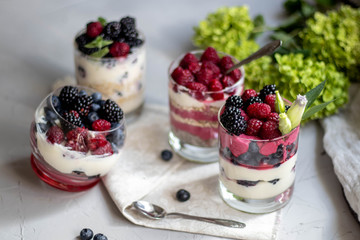 Healthy nutrition Dietary desserts. Glasses are filled with cottage cheese cream, in them chia seeds, raspberries, blueberries, blackberries. Near for background flowers.