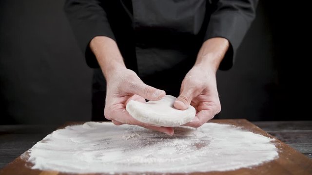 Cook prepares wheat dough for pizza on the black background