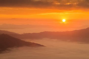 Mountain view misty morning of top hills around with sea of mist in valley and yellow sun light with cloudy sky background, sunrise at Pha Tang, Chiang Rai, northern of Thailand.
