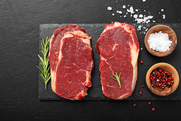 Fototapeta na wymiar Raw meat, beef steak with spices on black background, top view.