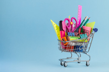 Shopping cart with different stationery on the light blue background