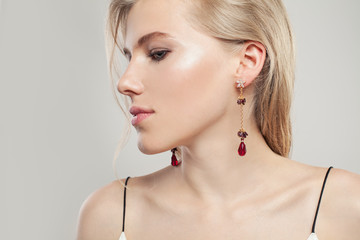 Gold jewelry model. Beautiful woman with fashion golden earrings with red garnet on white background
