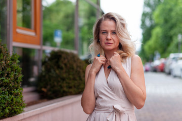 A blonde girl of European appearance in an evening dress poses in the city