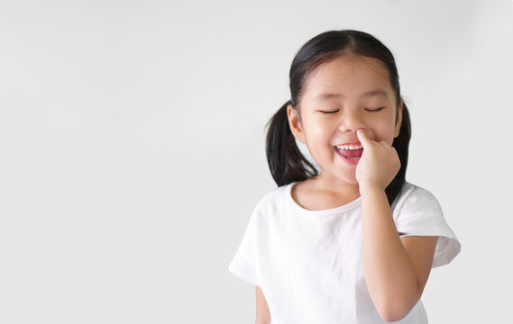 Asian child cute or kid girl enjoy nose picking or picky by finger with eat snot and smiling happy with close eye on preschool or 5 years old and wear white t-shirt on white background with copy space