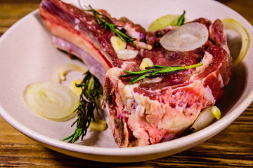 Raw ribeye steak, spices, rosemary, onion and garlic in a ceramic plate on wooden table