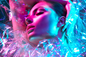Fashion model woman in colorful bright neon lights posing in studio through transparent film....