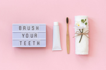 Brush your teeth - Light box text and natural eco-friendly bamboo brush for teeth, towel, toothpaste tube. Set for washing on pink background. Concept dental health care Top view Flat lay