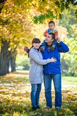 Family of three walks in the autumn park holding hands. happy father carrying son with maple leaves. Mother embrace her cute boy child. Happy family leisure together concept