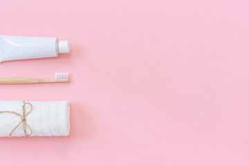 Natural eco-friendly bamboo brush, white towel and tube of toothpaste. Set for washing and brushing your teeth on pink background. Template for design Top view Flat lay Copy space