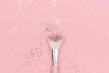 Makeup brush and shiny sparkles on pastel pink background. Festive magic makeup concept. Template...