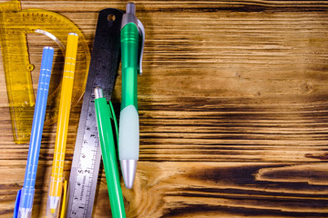 Multi colored ball pens, protractor and ruler on a wooden table. Top view
