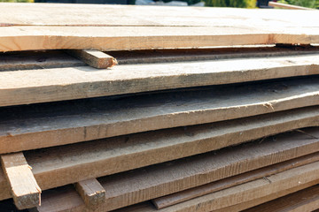 rough wooden boards lie in rows, boards for construction works, sunny weather. wooden planks lie in rows. eco friendly wood for construction.