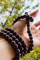 monk’s arm with mahogany rosary beads for meditation. sandalwood beads wrapped around male arm and fingers, selective focus, vertical image.
