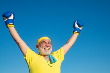 Happy Senior man wearing boxing gloves. Portrait of a determined senior boxer over blue sky...