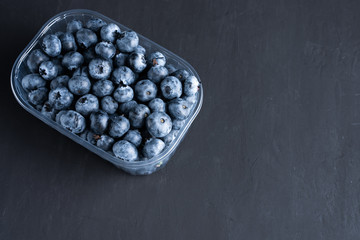Fototapeta na wymiar Tasty juicy raw blueberries in a plastic container on a black dark background.