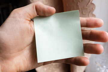 male hand holding a blank sticker. square paper with space for text in the hand of a young man, close-up. sticky note on a hand.