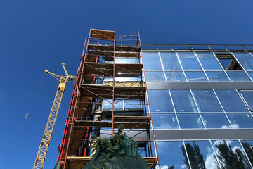 Scaffolding frame on a modern glass building and yellow Construction crane from the side, bottom view. reconstruction of an old public building in the city center. replacement of concrete walls