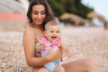 Portrait of cute baby girl with her mother on the beach. Mom with daughter in swimsuit by the sea. Happy baby