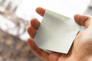 male hand holding a blank gray sticker. square paper with space for text in the hand of a young man, close-up. empty sticky note in a hand.