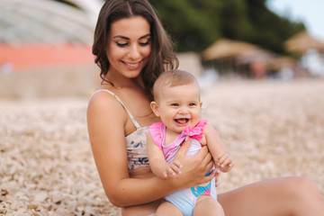 Portrait of cute baby girl with her mother on the beach. Mom with daughter in swimsuit by the sea. Happy baby