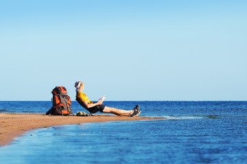 A man sits on a chair on the beach with a book and looks into the horizon. Near backpack and boots....