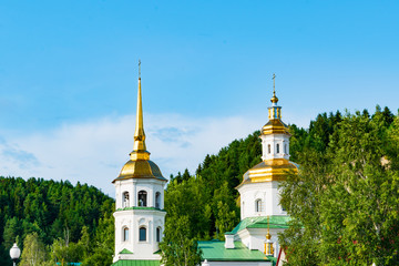 Fototapeta na wymiar A small modern Christian Orthodox Church, a temple in the city against the background of green trees and blue sky with clouds