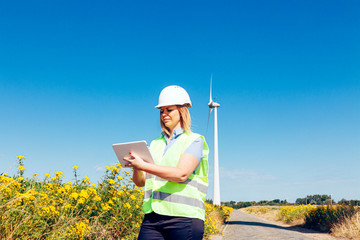 female wind engineer checking a tablet in a turbines field. renewable energy and job technology concept