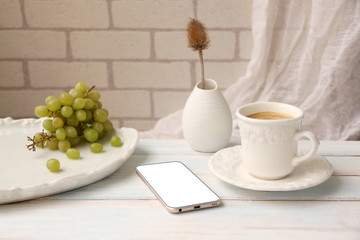 white blank for text on the smartphone on a white table and a white cup with coffee, grapes on a plate, the concept morning, top view, copy space