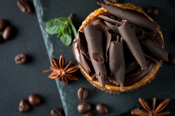 Chocolate cakes on black slatter board with mint, coffee beans on dark background, closeup photo. Fresh, tasty dessert food concept.