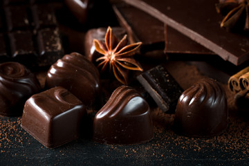Assortment of dark, white and milk chocolate stack, chips. Chocolate and coffee beans on rustic wooden sacking background. Spices, cinnamon. Selective macro focus. Chocolates background. Sweets