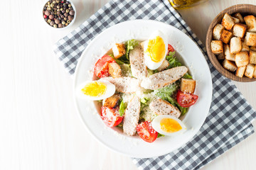 Fresh salad made of tomato, ruccola, chicken breast, eggs, arugula, crackers and spices. Caesar salad in a white, transparent bowl on wooden background