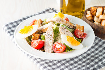 Fresh salad made of tomato, ruccola, chicken breast, eggs, arugula, crackers and spices. Caesar salad in a white, transparent bowl on wooden background