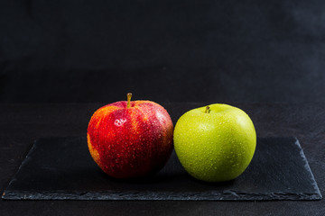 Red and green apples with dew drops on black background an black stone surface