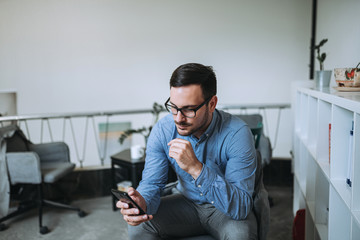 Caucasian man using phone in bright office.