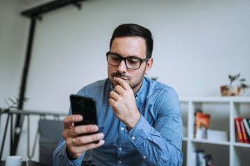 Young thoughtful man looking at mobile phone.