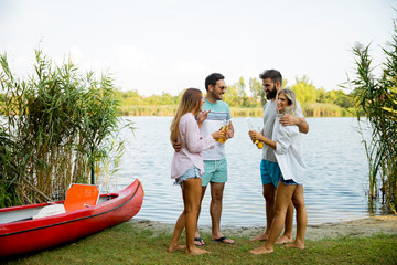 Obraz premium Group of friends with cider bottles standing by the boat near the beautiful lake and having fun